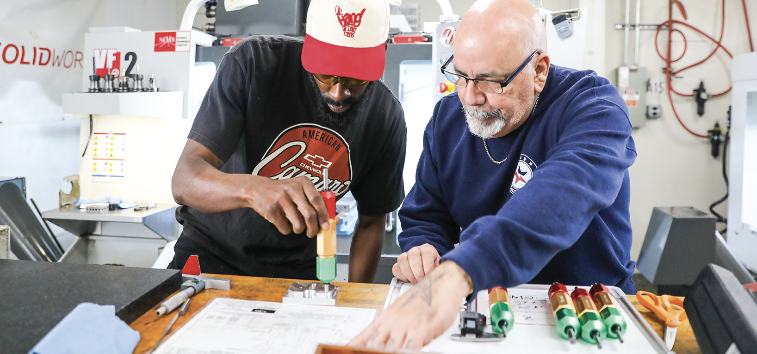 Student Anthony R. (left) with trainer and mentor Randall U. (right) going over the blueprint and verifying parts.